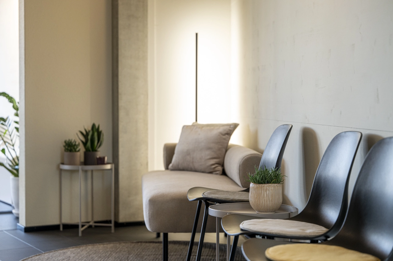 Gemütliche Sitzecke im Loungebereich von CHEETAH Health mit beigem Sofa, modernen Stühlen, Stehlampe und Dekopflanzen.