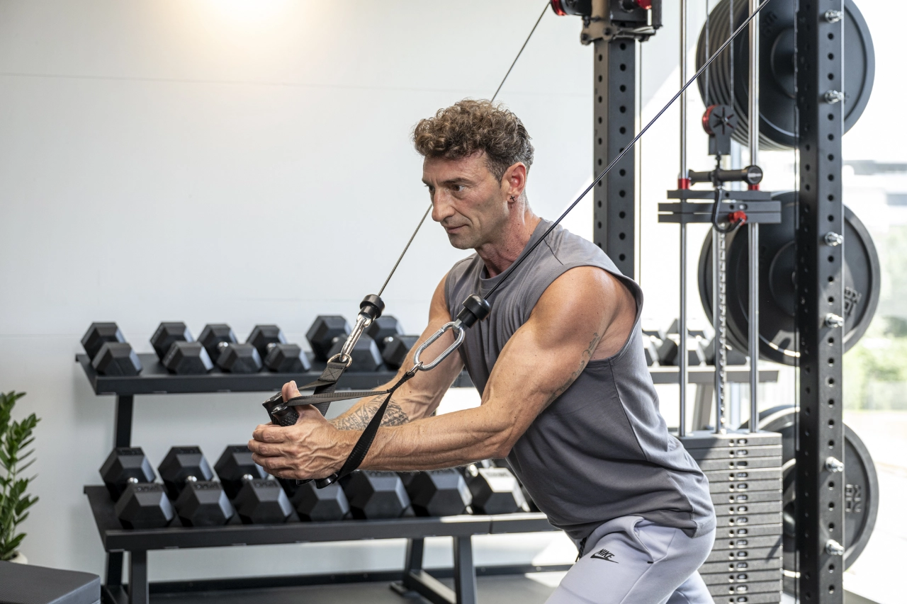 Ein durchtrainierter Mann in grauer Sportbekleidung führt im modernen Studio von CHEETAH Health konzentriert Cable Crossovers (Fliegende am Kabelzug) zur Stärkung der Brustmuskulatur aus.