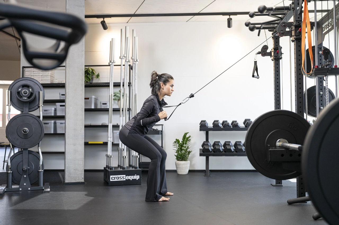 Eine Frau in dunkler Sportbekleidung führt barfuß eine Ruderübung am Kabelzug in leicht gehockter Haltung im Trainingsbereich von CHEETAH Health aus.
