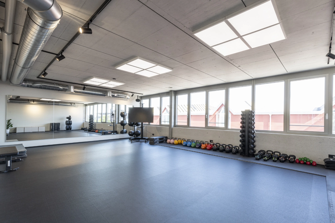 Weitläufiger, lichtdurchfluteter Kurs- und Trainingsraum im Studio von CHEETAH Health mit großer Spiegelwand, Fensterefront und aufgereihten Kettlebells sowie Kurzhanteln.